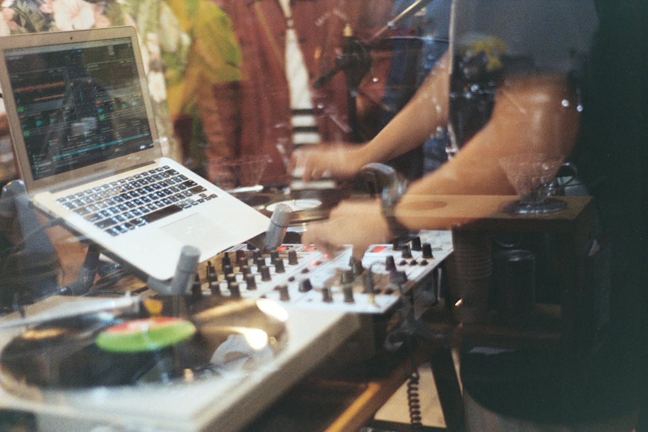 DJ playing vinyl records with hands on mixing panel and laptop in a studio.